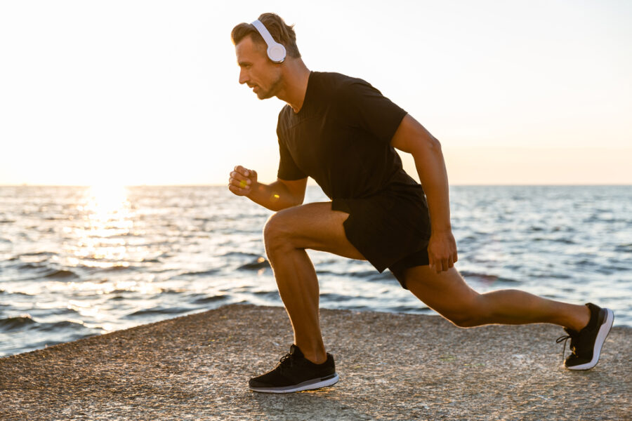 Man with headphones doing lunges on a beach