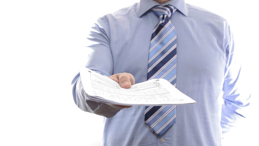 Man in dress shirt and tie handing a stack of papers toward camera.