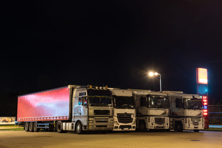 Semi-trucks parked in row at truck stop at night.