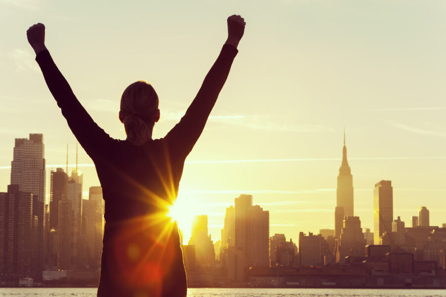Person raising hands in victory in front of city skyline at sunrise