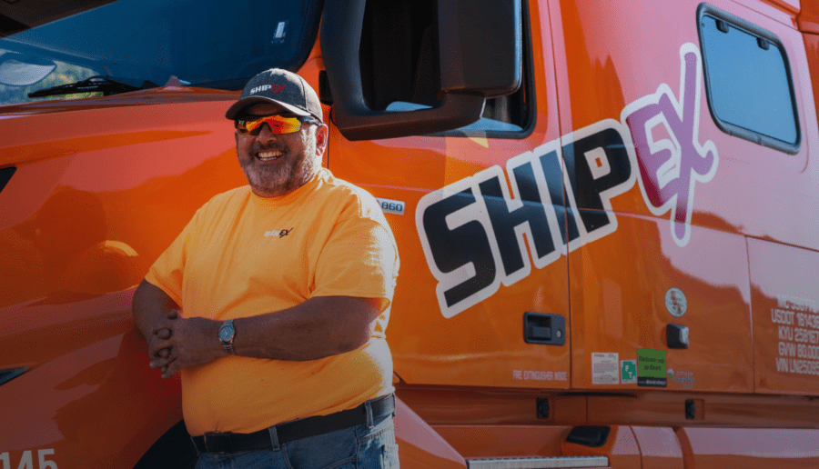 Truck Driver leaning on orange ShipEX semi-truck