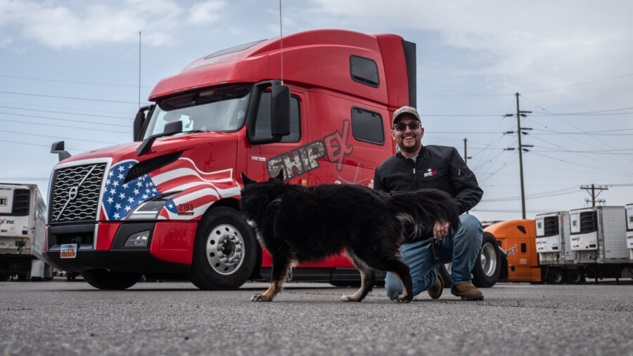 truck driver kneeling in front of red truck with dog