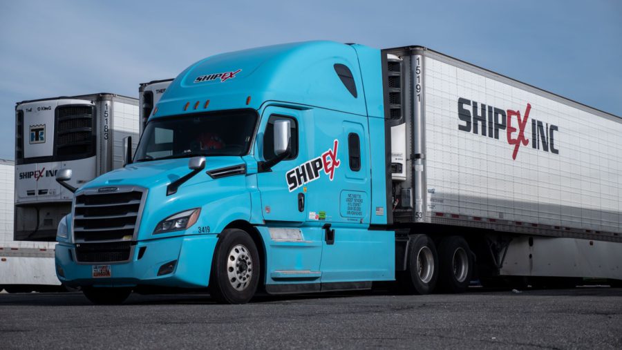 Light blue ShipEX semi-truck in front of row of refrigerated trailers.