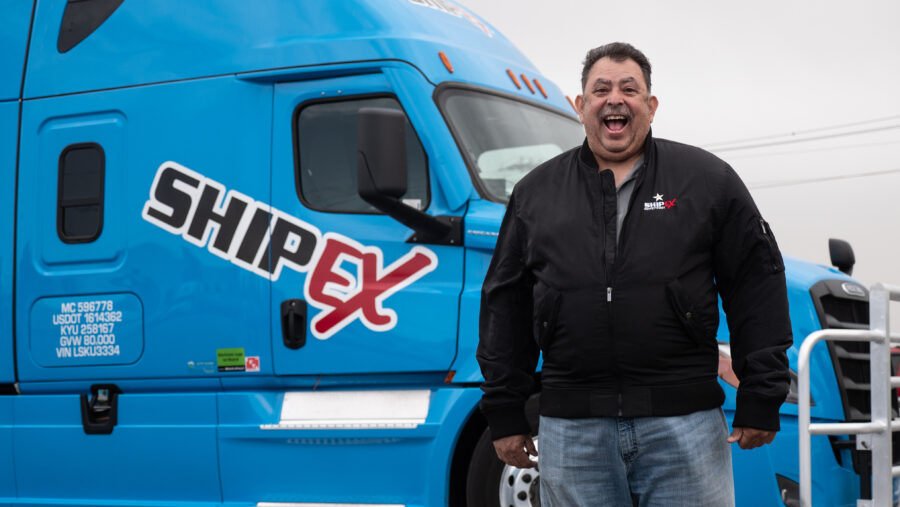 truck driver smiling wide in front of a blue semi truck