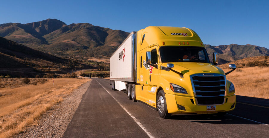 yellow ShipEX semi truck and trailer driving down desert road