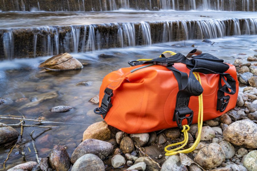 small waterproof duffel on a rocky river shore below a dam