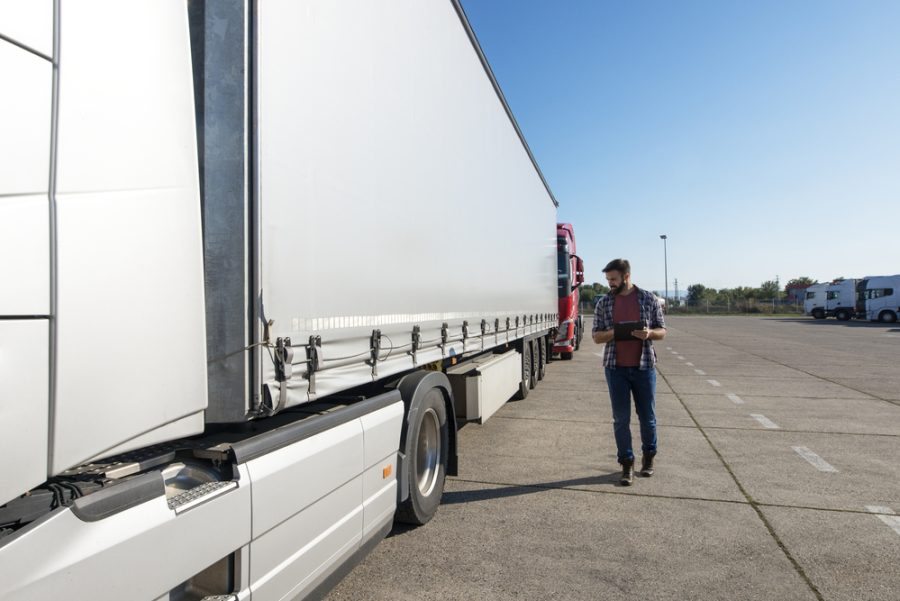 Truck driver inspecting vehicle, trailer and tires before driving. Truck preparation before ride. Transportation services.