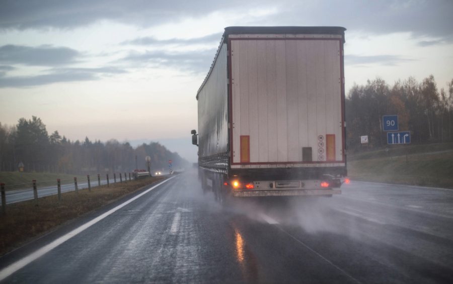 A truck with a trailer is being rebuilt on a motorway in a different row on slippery wet roads. The concept of security and attention to roads in bad weather, rain, accident