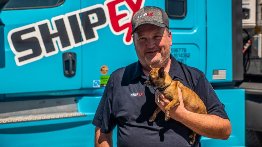 Truck driver holding dog in front of blue truck