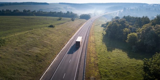 truck along empty highway surrounded by grass and trees