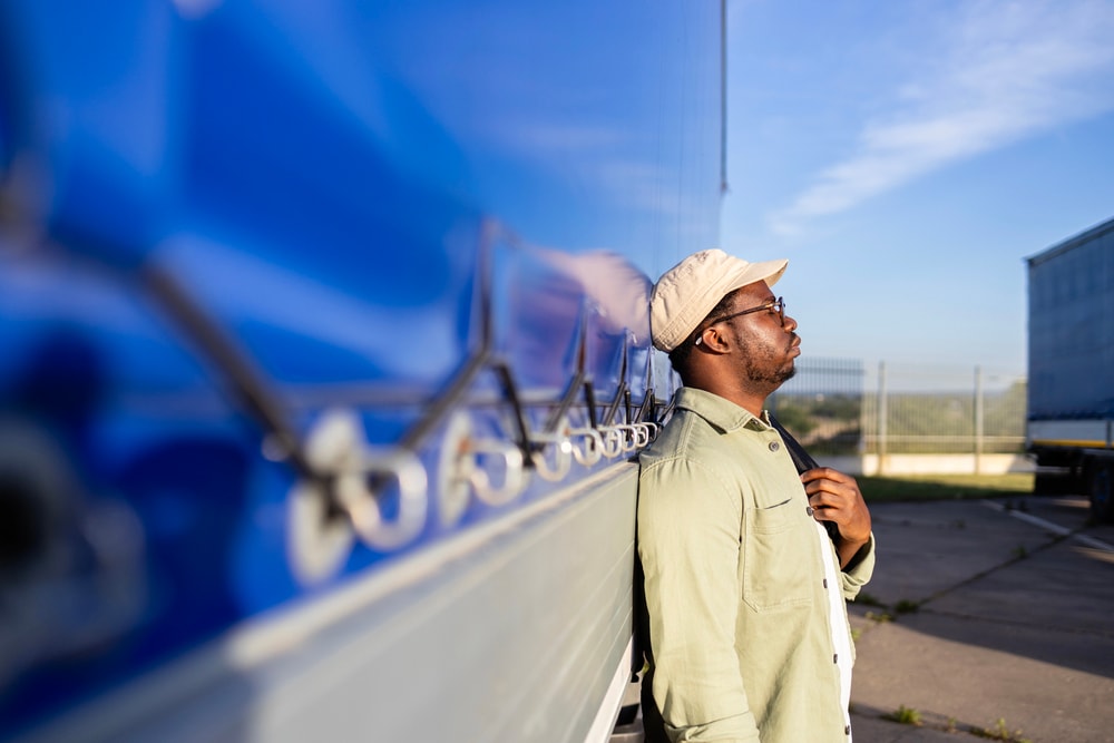 Stressed truck driver leaning against trailer